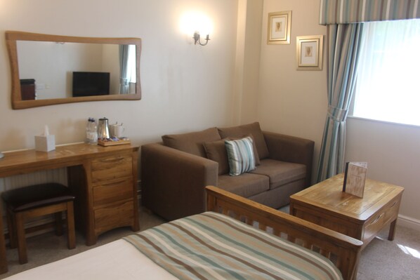 A hotel room with a bed, a wooden desk, a brown sofa, a small wooden table, and a mirror on the wall. - Nant Ddu Lodge Hotel & Spa by Belvilla (Merthyr Tydfil)