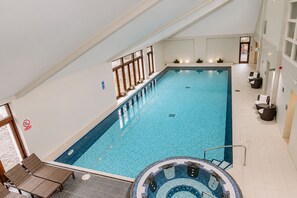 A large indoor swimming pool with a clear blue water, a hot tub area, and a seating area with chairs and tables. - Nant Ddu Lodge Hotel & Spa by Belvilla (Merthyr Tydfil)