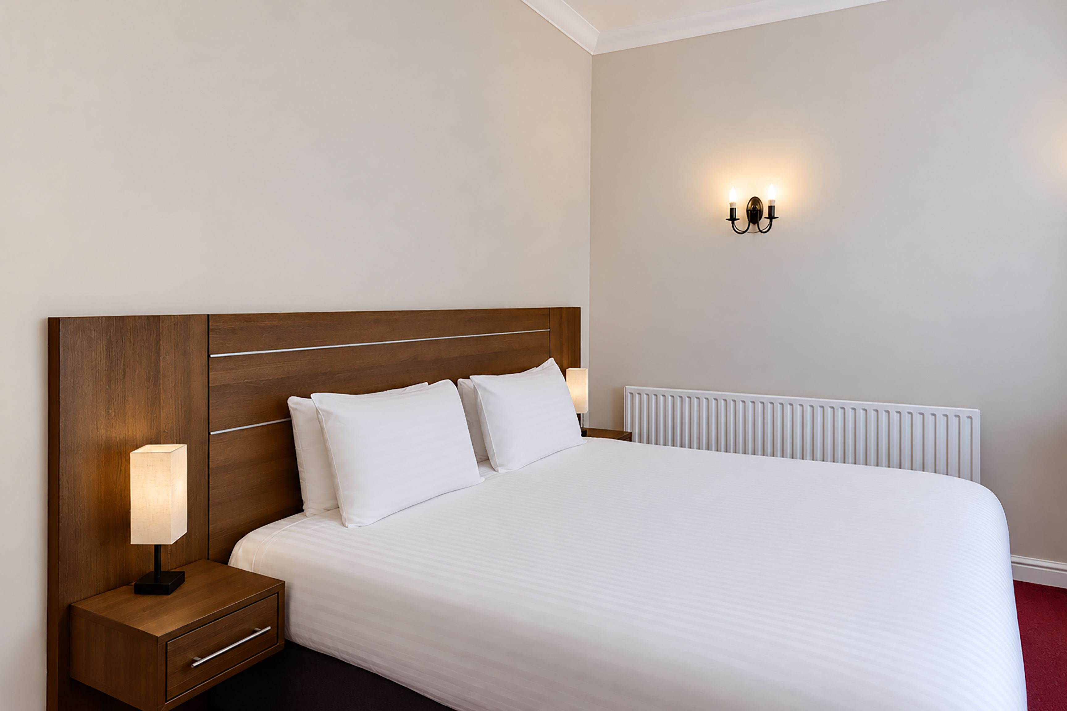 Une chambre d’hôtel avec un grand lit, une table de chevet, un luminaire fixé au mur et un radiateur.