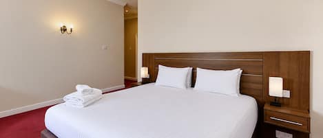 A neatly made bed with white linens, two bedside lamps, and a folded towel on the footboard.