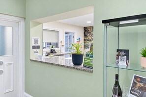Een receptiezone met een balie, een spiegel die het interieur weerspiegelt, een glazen display met een fles en glas, en een bord met een QR-code.