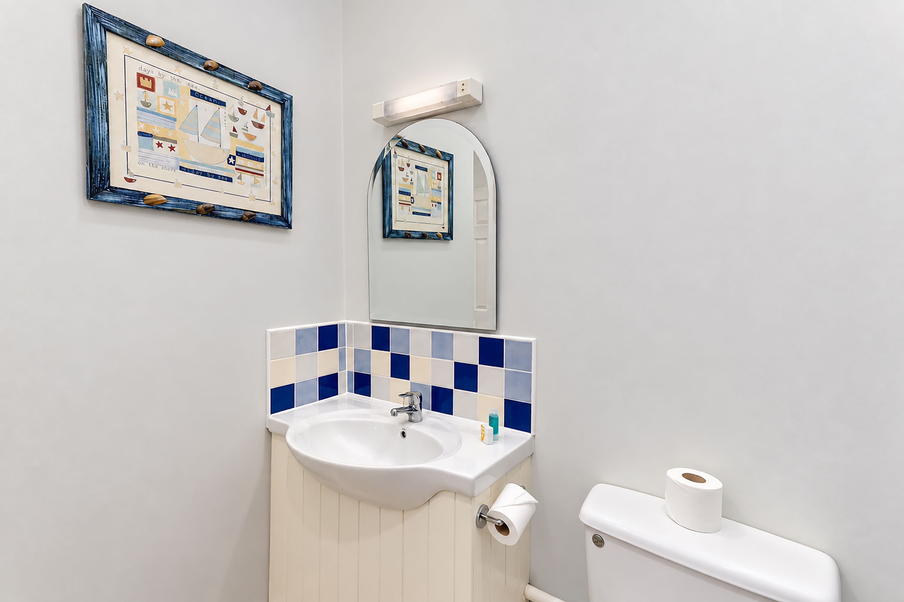 A bathroom with a sink, mirror, toilet, and two framed pictures on the wall.