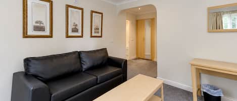 A room with a black leather sofa, a wooden table, and three framed pictures on the wall.