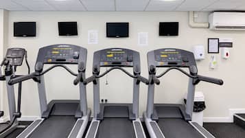 Drei Laufbänder in einem Fitnessstudio mit an der Wand montierten Fernsehern und einem Handdesinfektionsmittelspender.