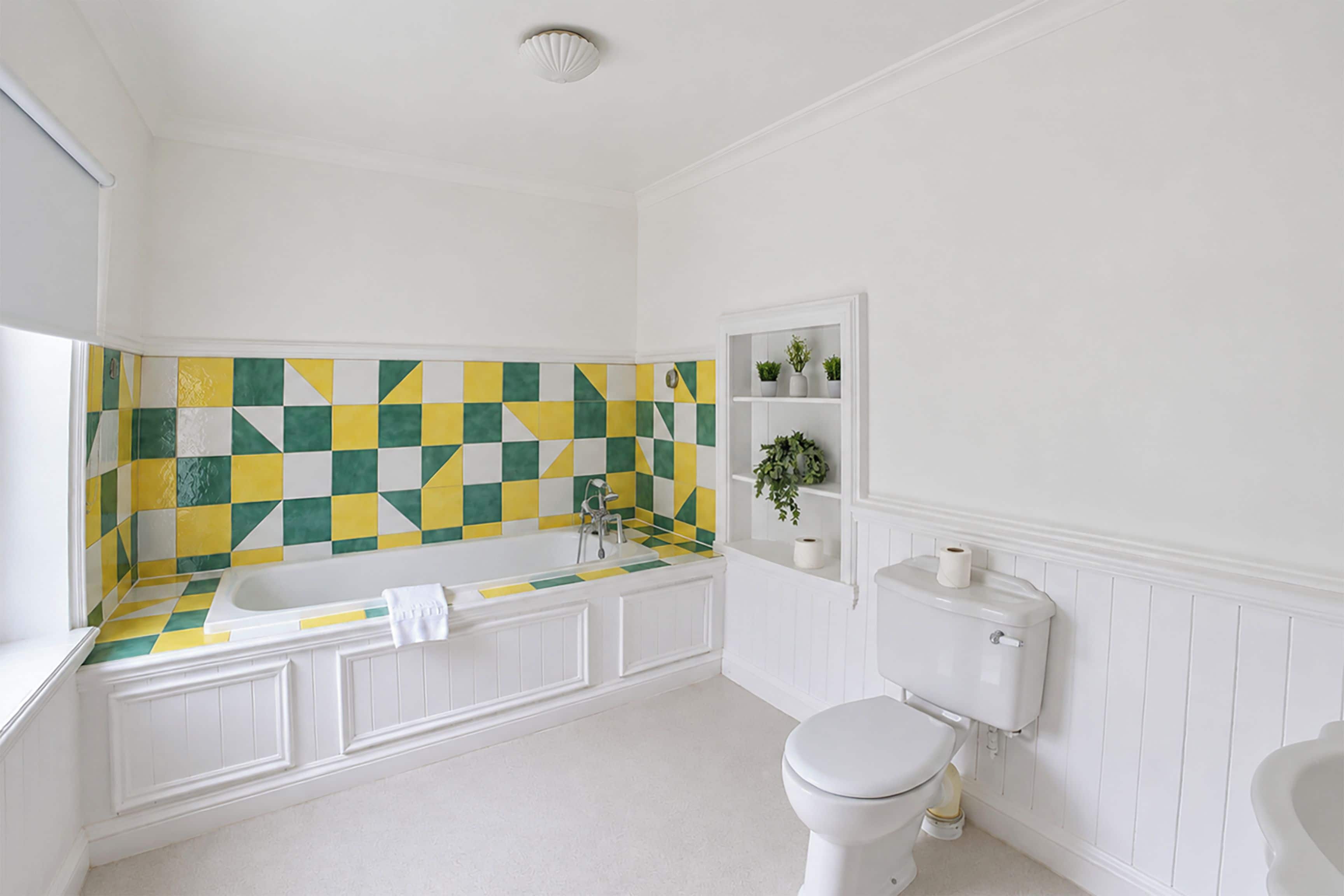 A bathroom with a white bathtub, a toilet, and a sink. There is a checkered tile backsplash above the bathtub.