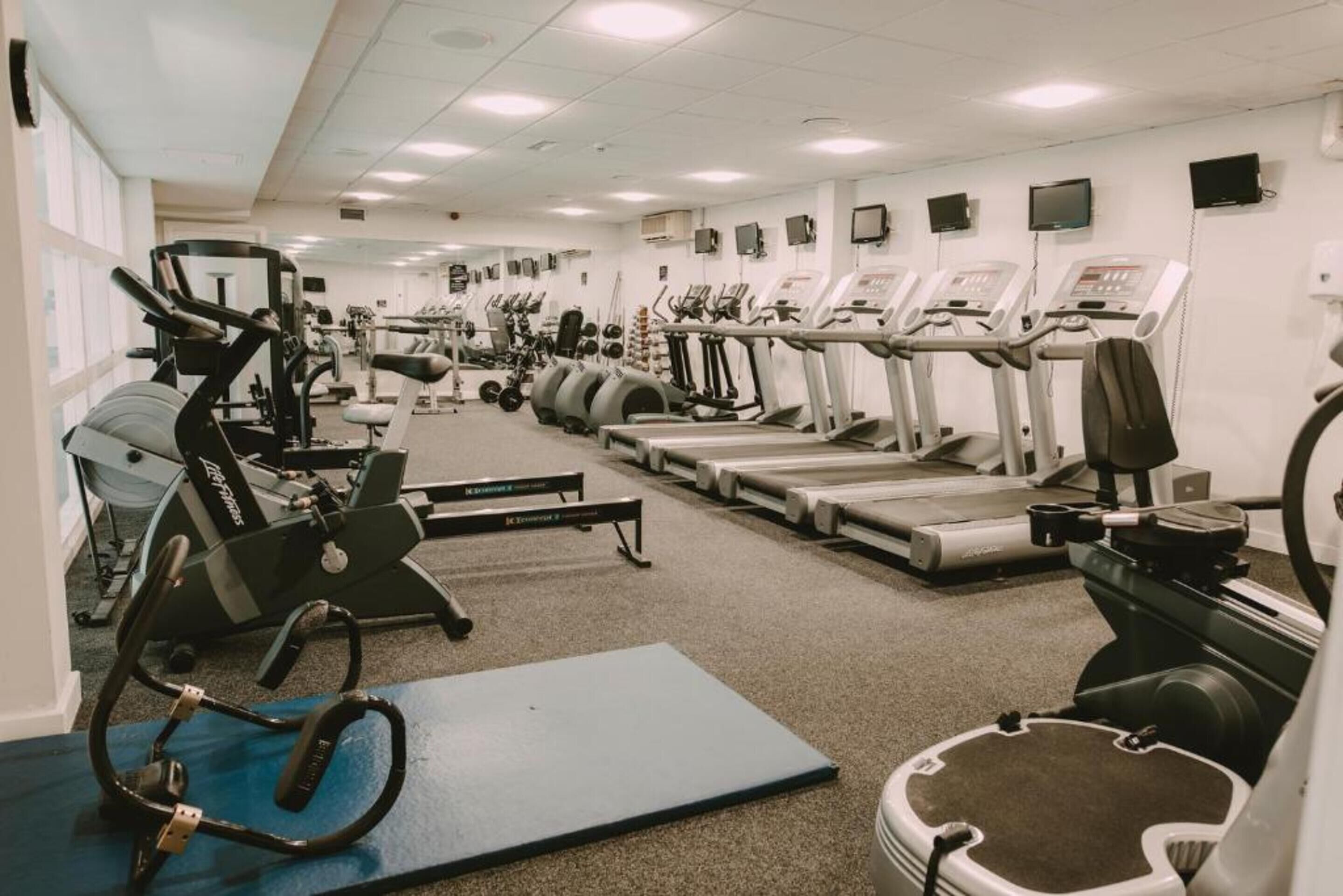 Un gimnasio con diversos equipos de ejercicio, incluyendo cintas de correr, elípticas y máquinas de pesas.