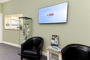 A reception area with a glass display case, a television mounted on the wall, and two black leather chairs. - Nant Ddu Lodge Hotel & Spa by Belvilla (Merthyr Tydfil)