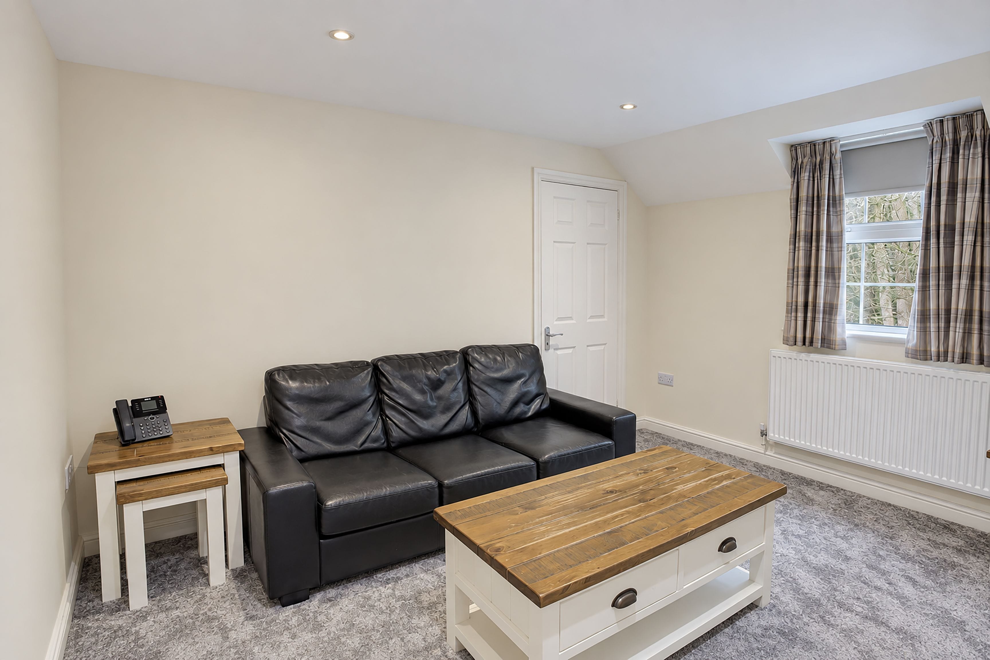A living room with a black leather sofa, a small wooden table, and a coffee table with a wooden top.