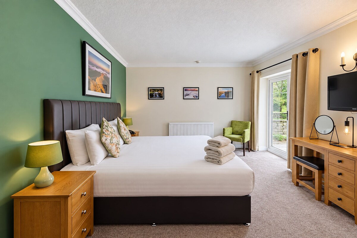 A hotel room with a bed, bedside tables, a desk, a chair, a television, and framed pictures on the wall.