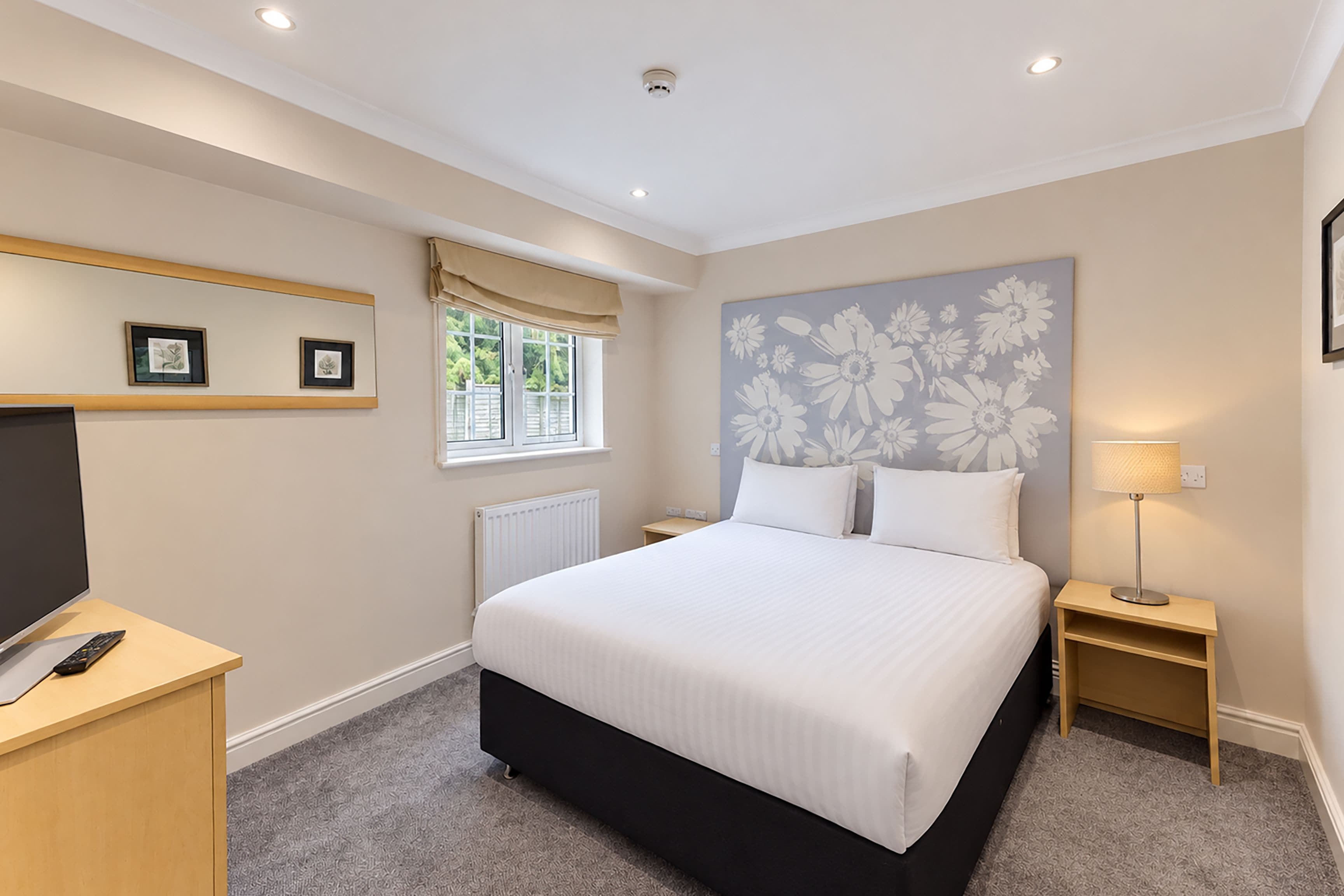 A bedroom with a bed, bedside tables, a TV, and a window with curtains.