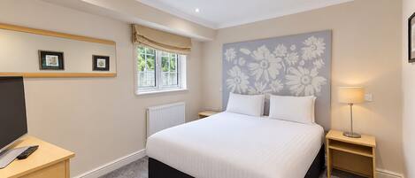A bedroom with a bed, bedside tables, a TV, and a window with curtains.