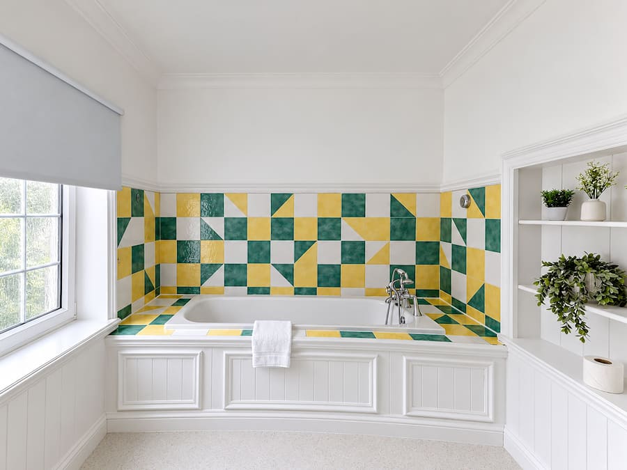 Un baño con salpicadero de azulejos a cuadros, una bañera blanca y estanterías empotradas con plantas.