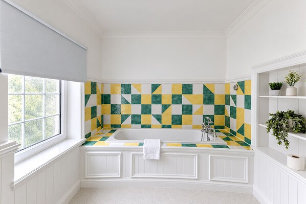 A bathroom with a checkered tile backsplash, a white bathtub, and built-in shelving with plants. - Nant Ddu Lodge Hotel & Spa by Belvilla (Merthyr Tydfil)