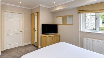 A bedroom with a bed, a television on a wooden cabinet, a mirror, and a window with a view of the outside.