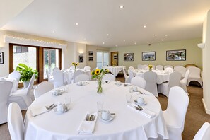A dining area with round tables, white chairs, and sunflowers in vases. - Nant Ddu Lodge Hotel & Spa by Belvilla (Merthyr Tydfil)