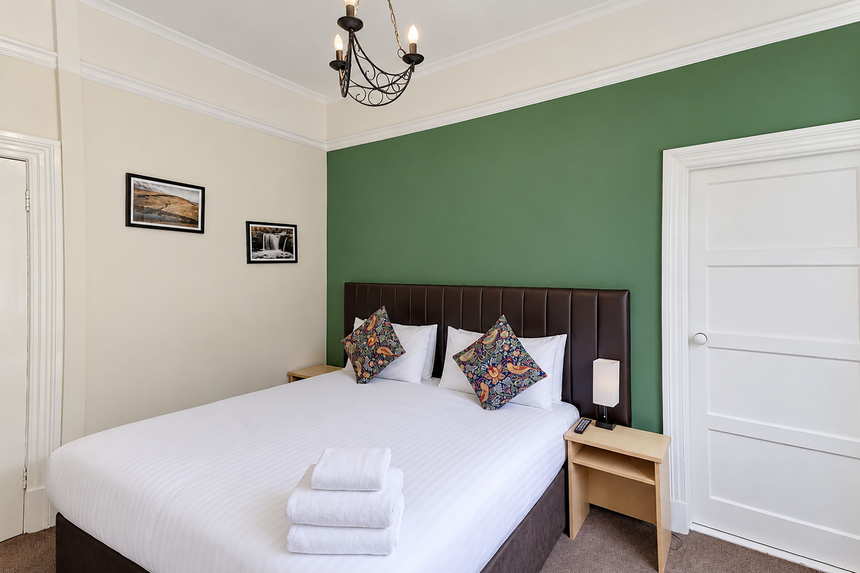 Ein Hotelzimmer mit einem großen Bett, zwei Kissen, einem Nachttisch, einer Lampe und einer Tür.