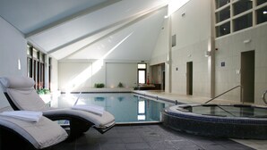 Een modern binnenzwembad met loungebedden, een jacuzzi en duidelijke borden voor de toiletten.