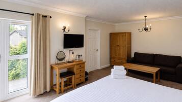 Habitación de hotel con cama, escritorio con espejo, televisor, armario, sofá y ventana con cortinas.