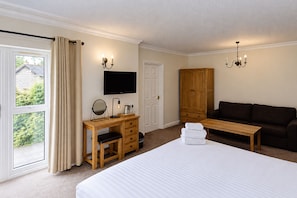 A hotel room with a bed, a desk with a mirror, a television, a wardrobe, a sofa, and a window with curtains. - Nant Ddu Lodge Hotel & Spa by Belvilla (Merthyr Tydfil)