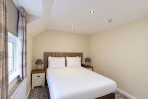 A hotel room with a large bed, two bedside tables with lamps, a window with curtains, and a ceiling with recessed lighting. - Nant Ddu Lodge Hotel & Spa by Belvilla (Merthyr Tydfil)