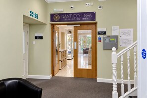 A hallway leading to a spa area with a fire exit sign, a thermostat, and a security camera. - Nant Ddu Lodge Hotel & Spa by Belvilla (Merthyr Tydfil)