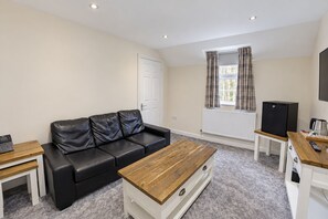 A furnished living room with a black leather sofa, a wooden coffee table, a white cabinet, a television, and a radiator. - Nant Ddu Lodge Hotel & Spa by Belvilla (Merthyr Tydfil)