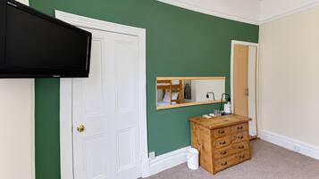 A room with a white door, a mounted television, a wooden dresser, and a mirror on the wall.