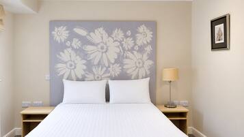 A hotel room with a large bed, two nightstands, a wall-mounted lamp, and a framed picture on the wall.