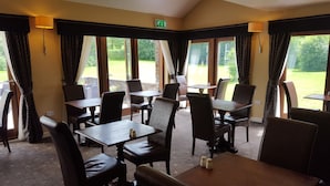 Een restaurant met tafels en stoelen klaar voor diners. Grote ramen bieden uitzicht op het omliggende landschap.