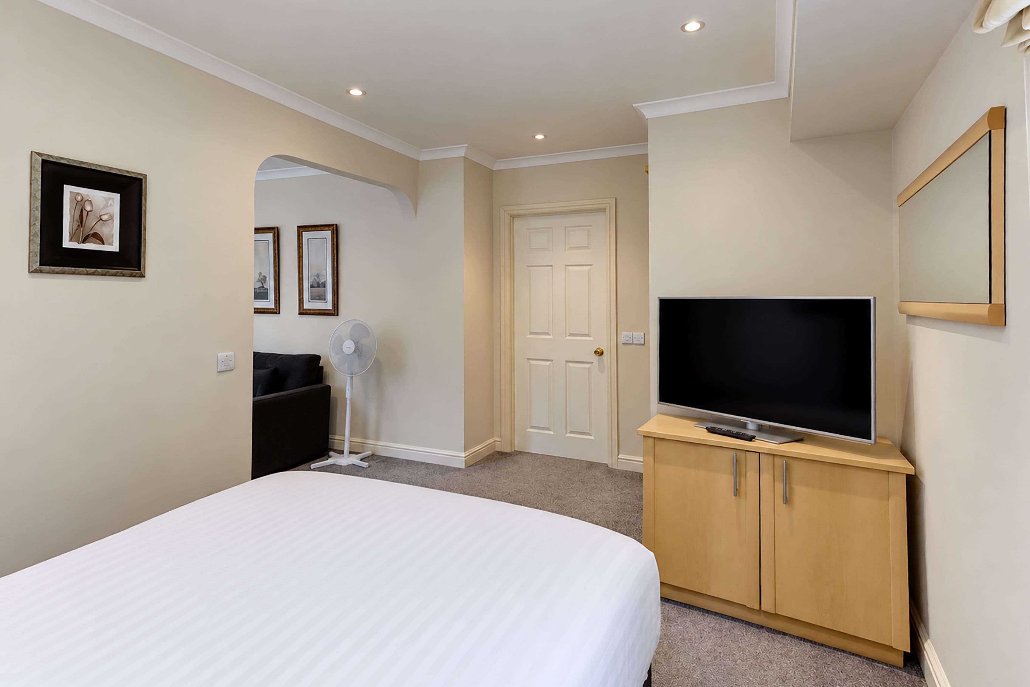 Ein Hotelzimmer mit einem Bett, einem Fernseher auf einer Holzkommode, einer Tür und einem Wandbild.