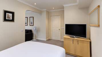 Ein Hotelzimmer mit einem Bett, einem Fernseher auf einer Holzkommode, einer Tür und einem Wandbild.