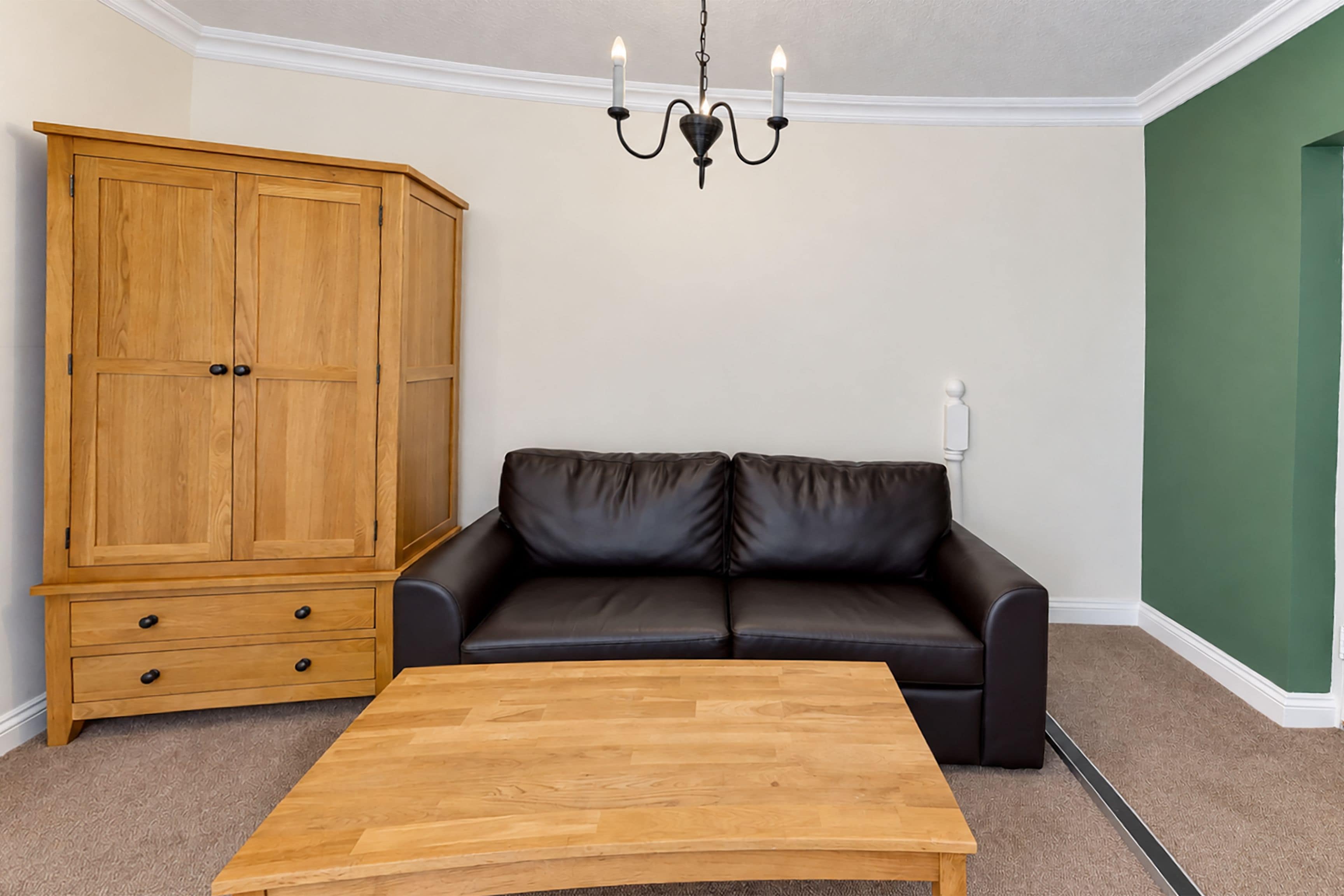 Ein Zimmer mit einem Holzkasten, einem schwarzen Ledersofa und einem Holztisch.