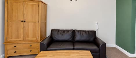 A room with a wooden cabinet, a black leather sofa, and a wooden coffee table.