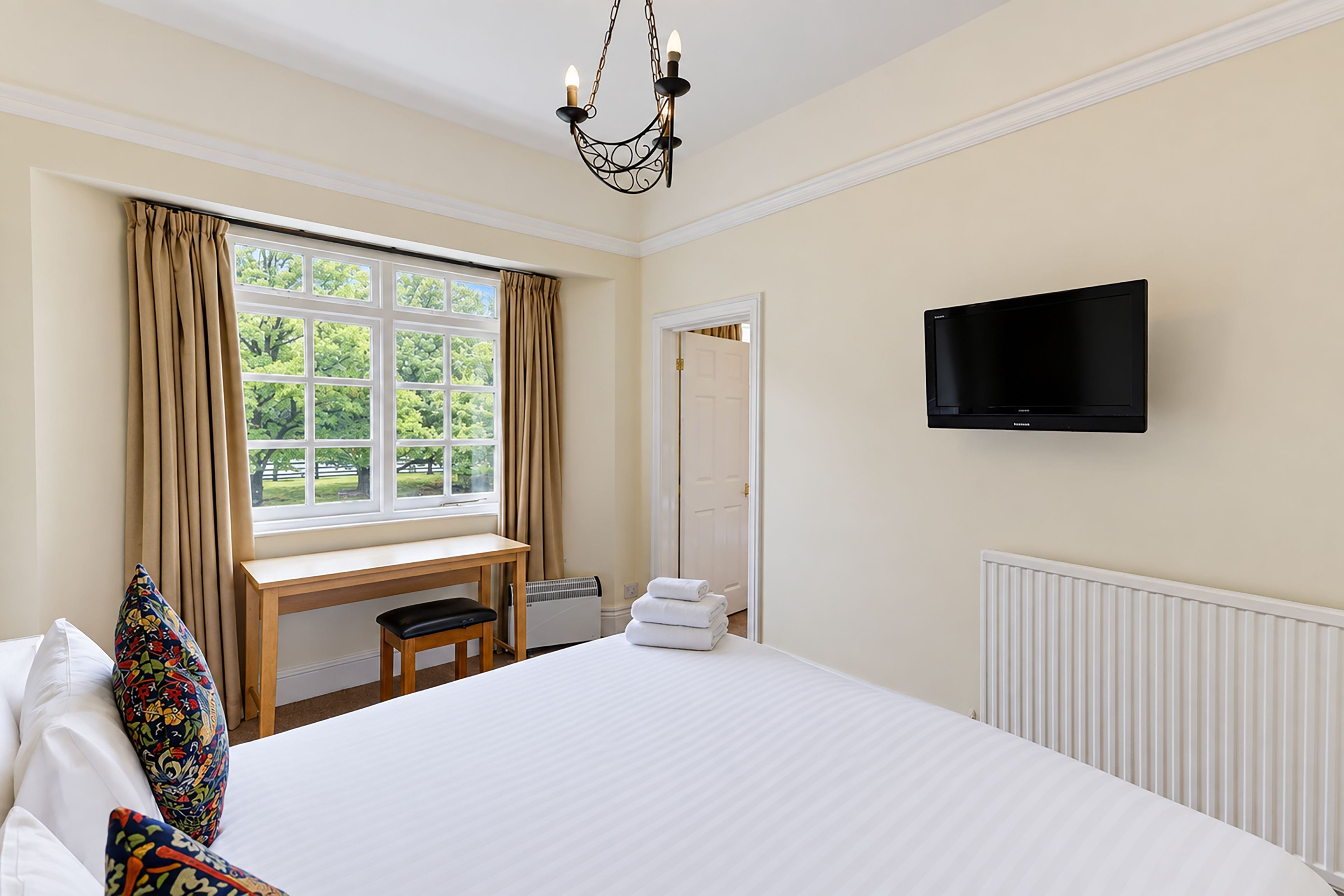 A hotel room with a large bed, a desk, a chair, a television, and a window with curtains.