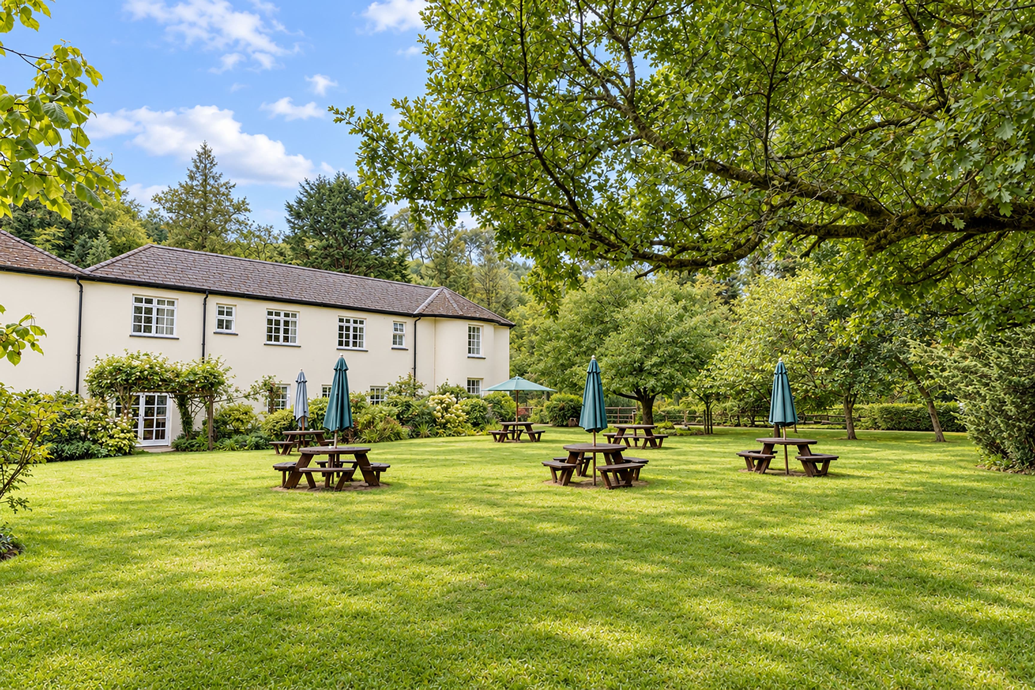 A large building with a white facade and a pitched roof, surrounded by a well-maintained lawn with picnic tables and umbrellas.