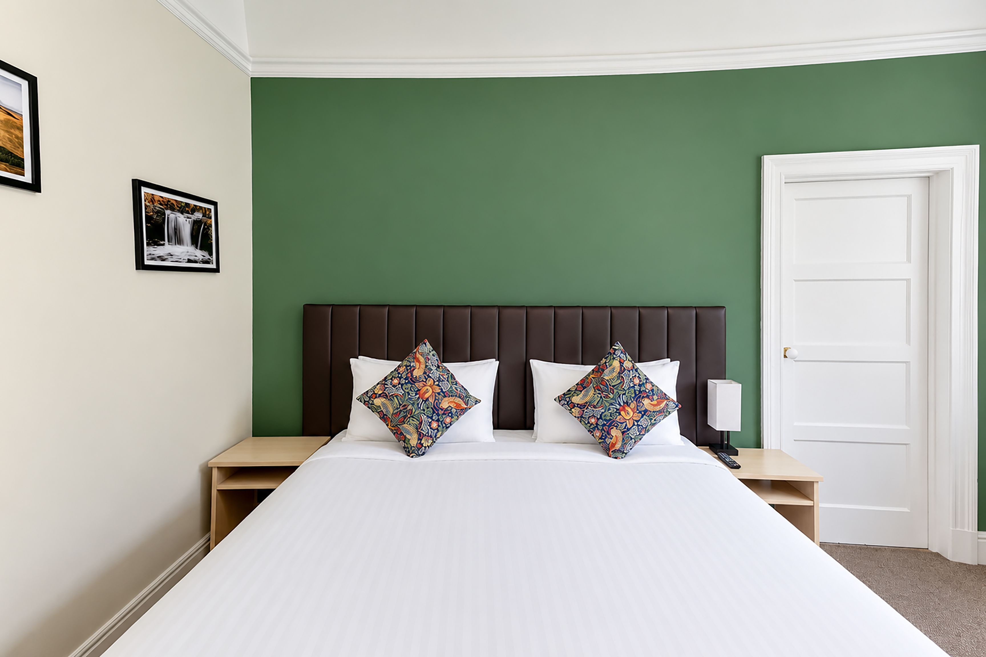 A hotel room with a large bed, two nightstands, a white door, and green walls.