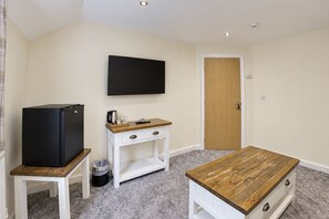 A compact room with a kitchenette, a flat-screen TV mounted on the wall, a wooden table, and a door. - Nant Ddu Lodge Hotel & Spa by Belvilla (Merthyr Tydfil)
