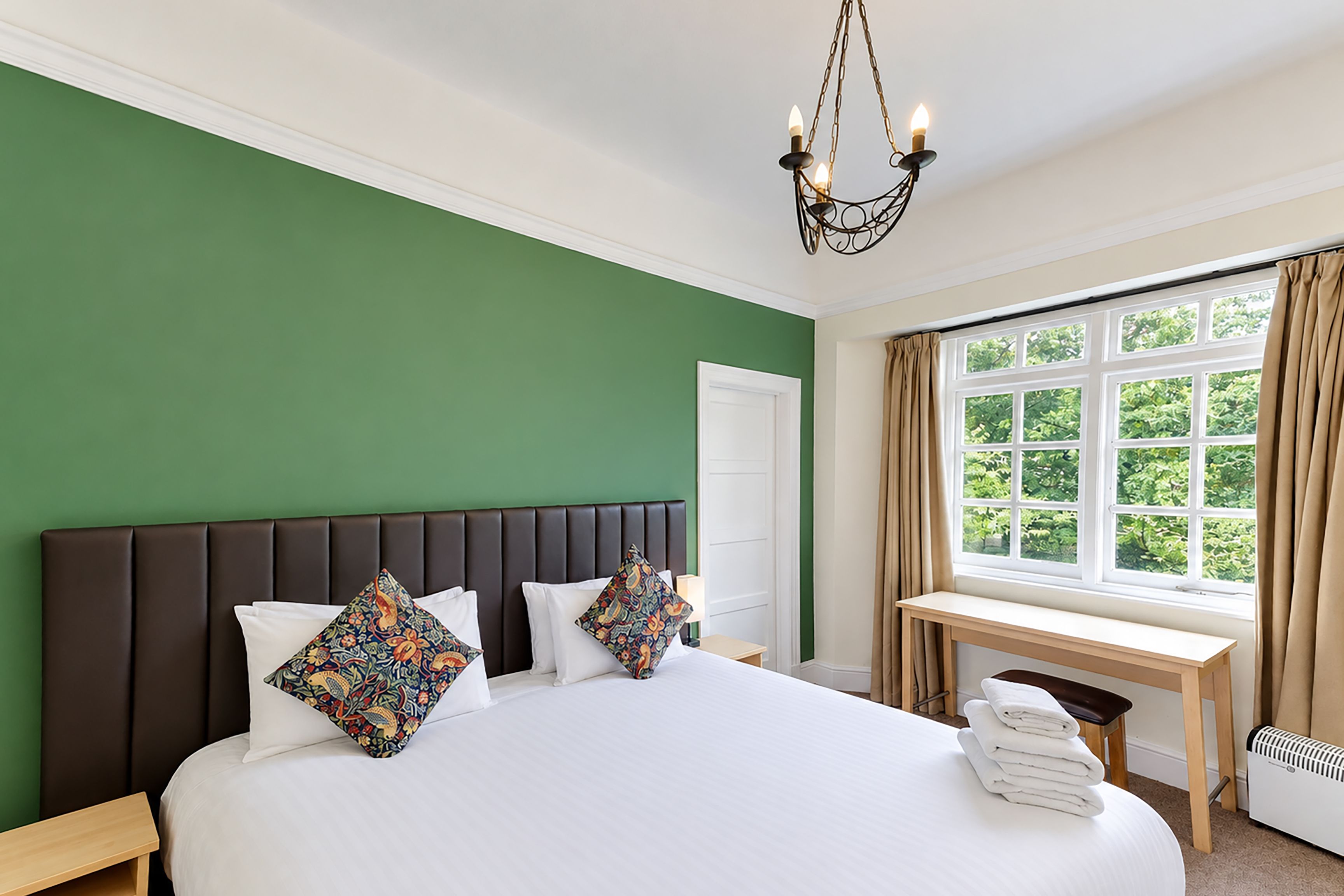 A hotel room with a large bed, a window with curtains, a bedside table, and a radiator.