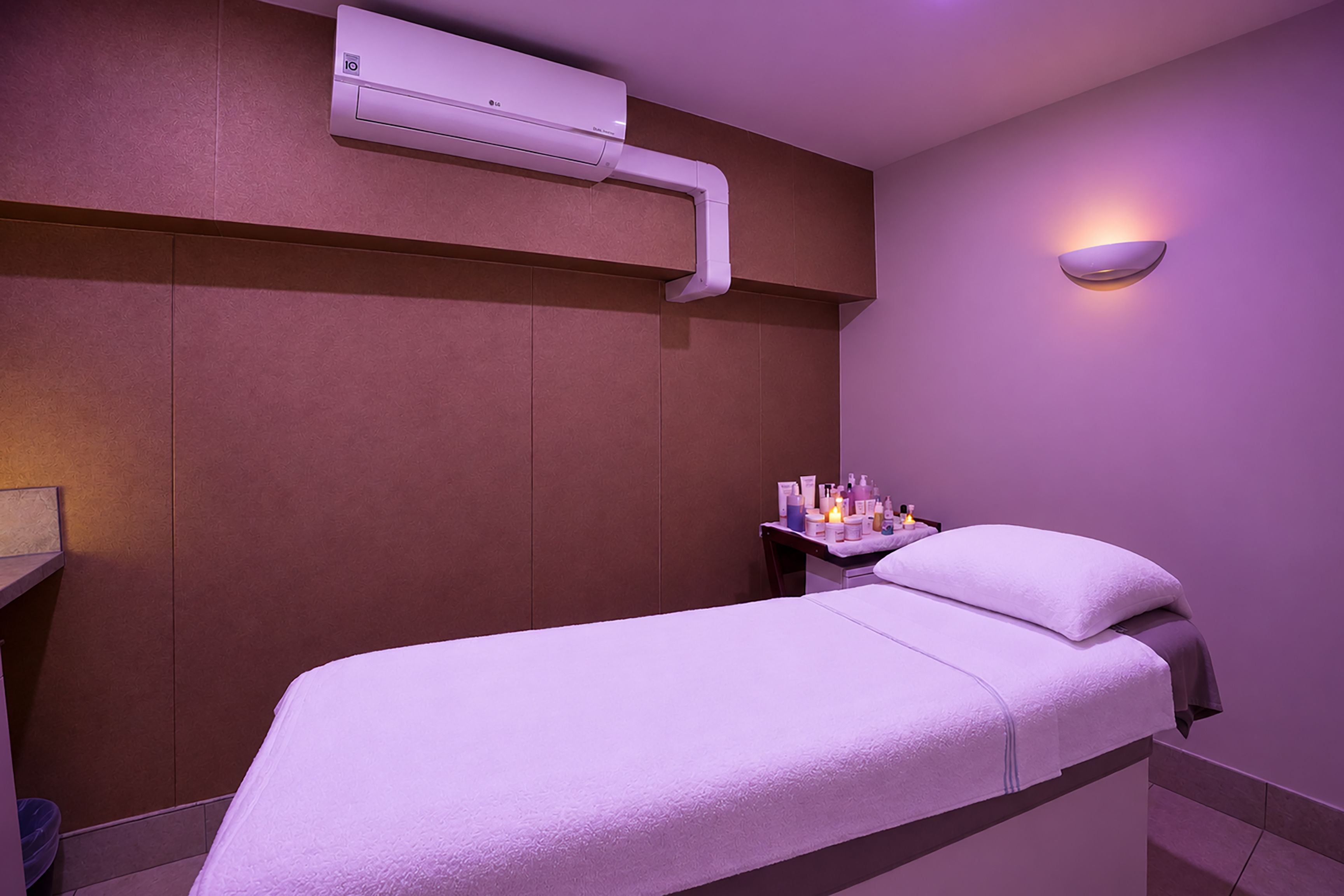 A room with a bed, a nightstand, a wall-mounted air conditioner, and a wall-mounted light fixture.