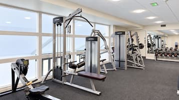 A gym with various exercise machines, large windows, and a carpeted floor.