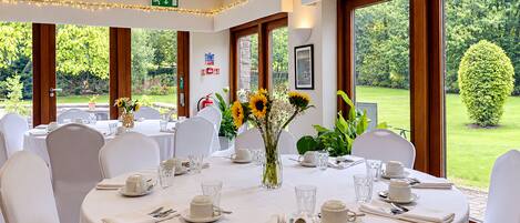 A dining area with round tables set for a meal, white tablecloths, and chairs.
