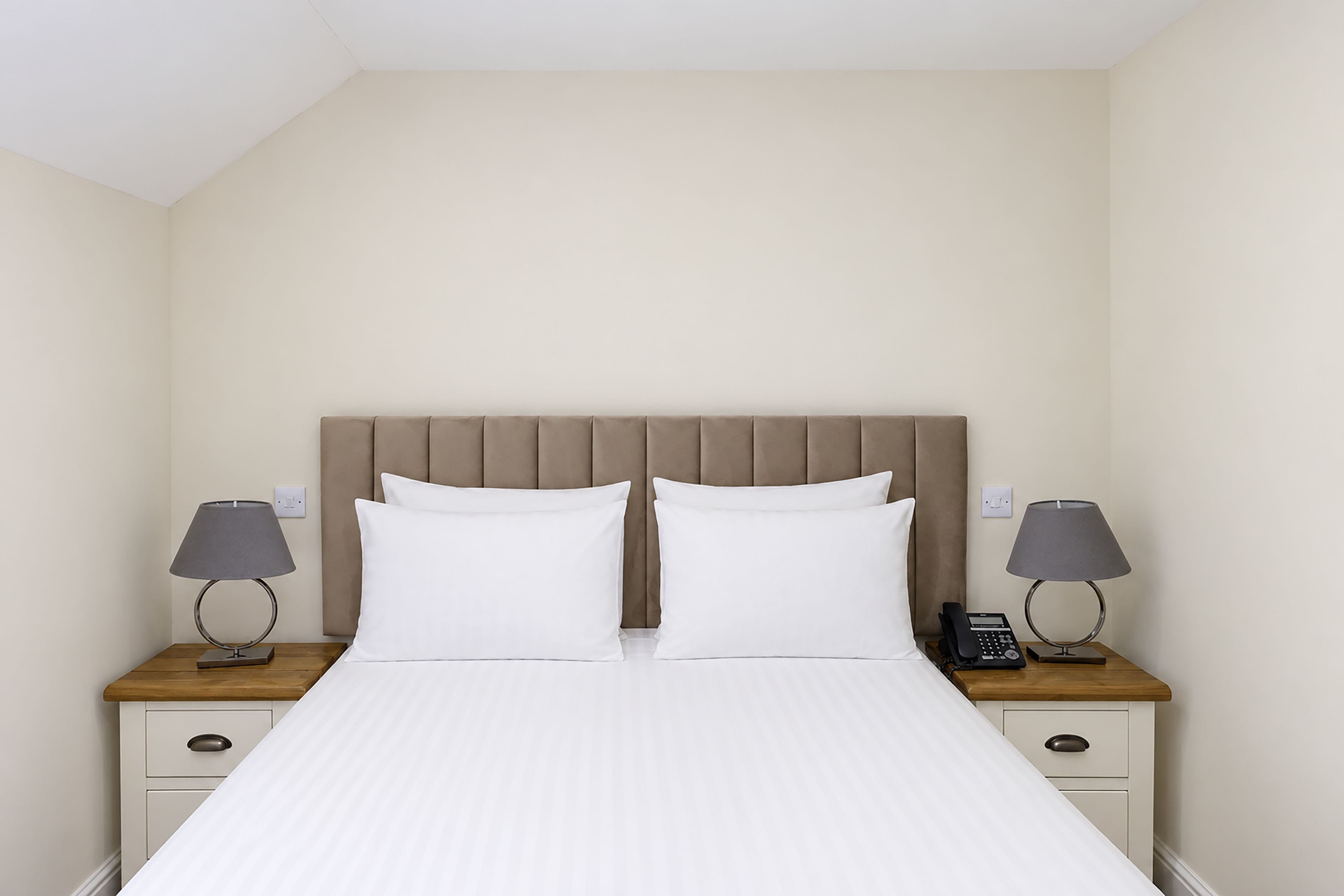 Ein Hotelzimmer mit einem Bett, zwei Nachttischen, einem Telefon und einer Lampe auf jeder Seite.