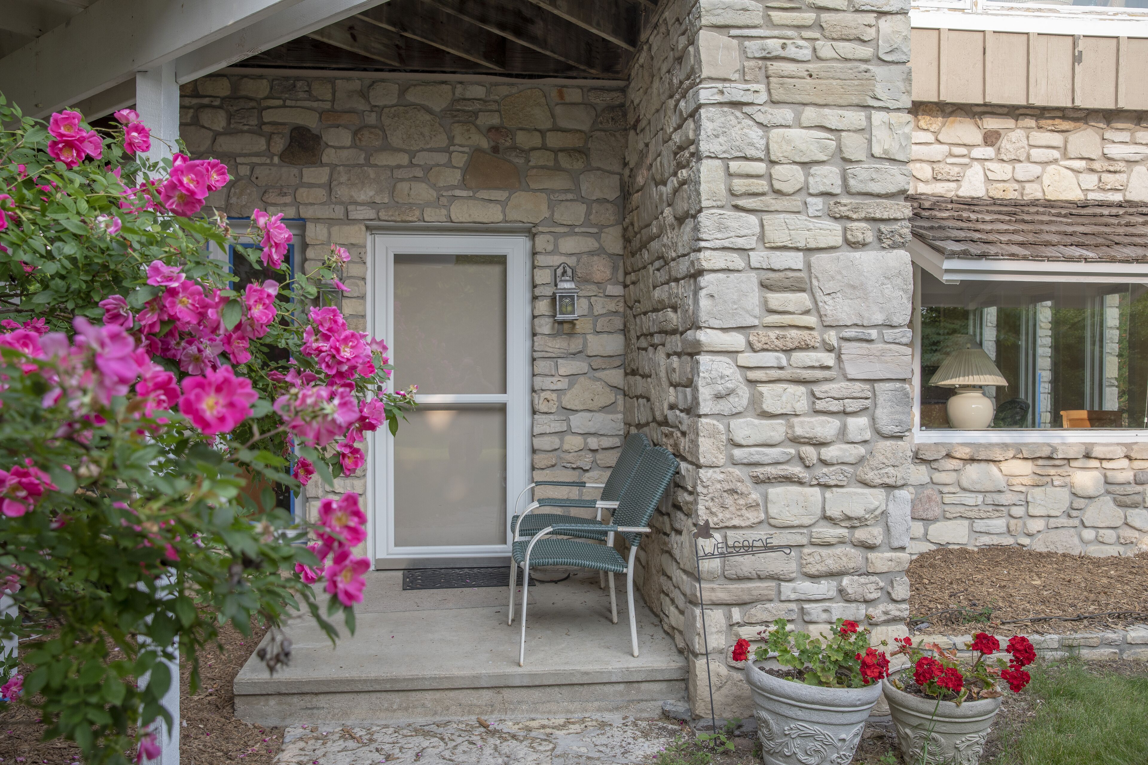 A stone building with a porch, a chair, and potted plants.