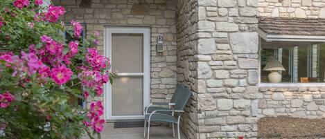 A stone building with a porch, a chair, and potted plants.