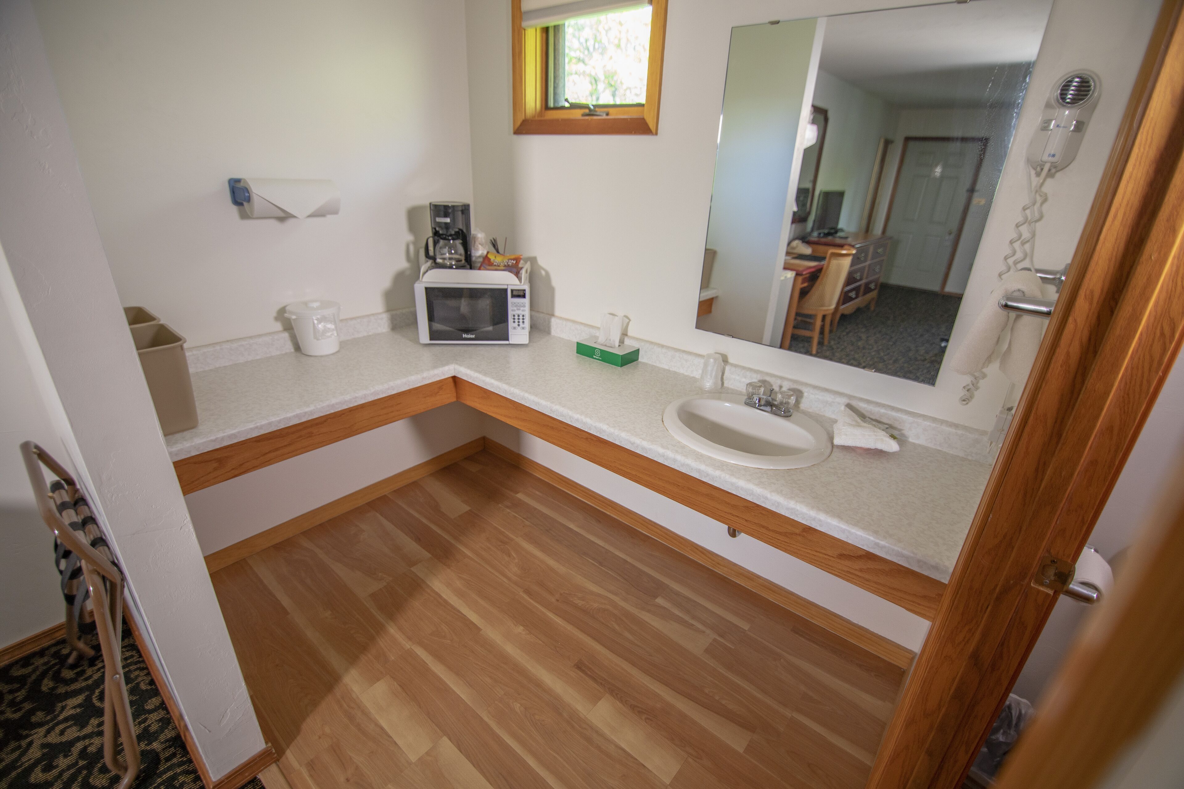 Une salle de bain avec un plancher en bois, un lavabo blanc, un miroir, un sèche-cheveux et un four à micro-ondes.