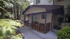 A covered patio area with a bench and table, surrounded by trees and a house. - Coachlite Inn (Sister Bay)