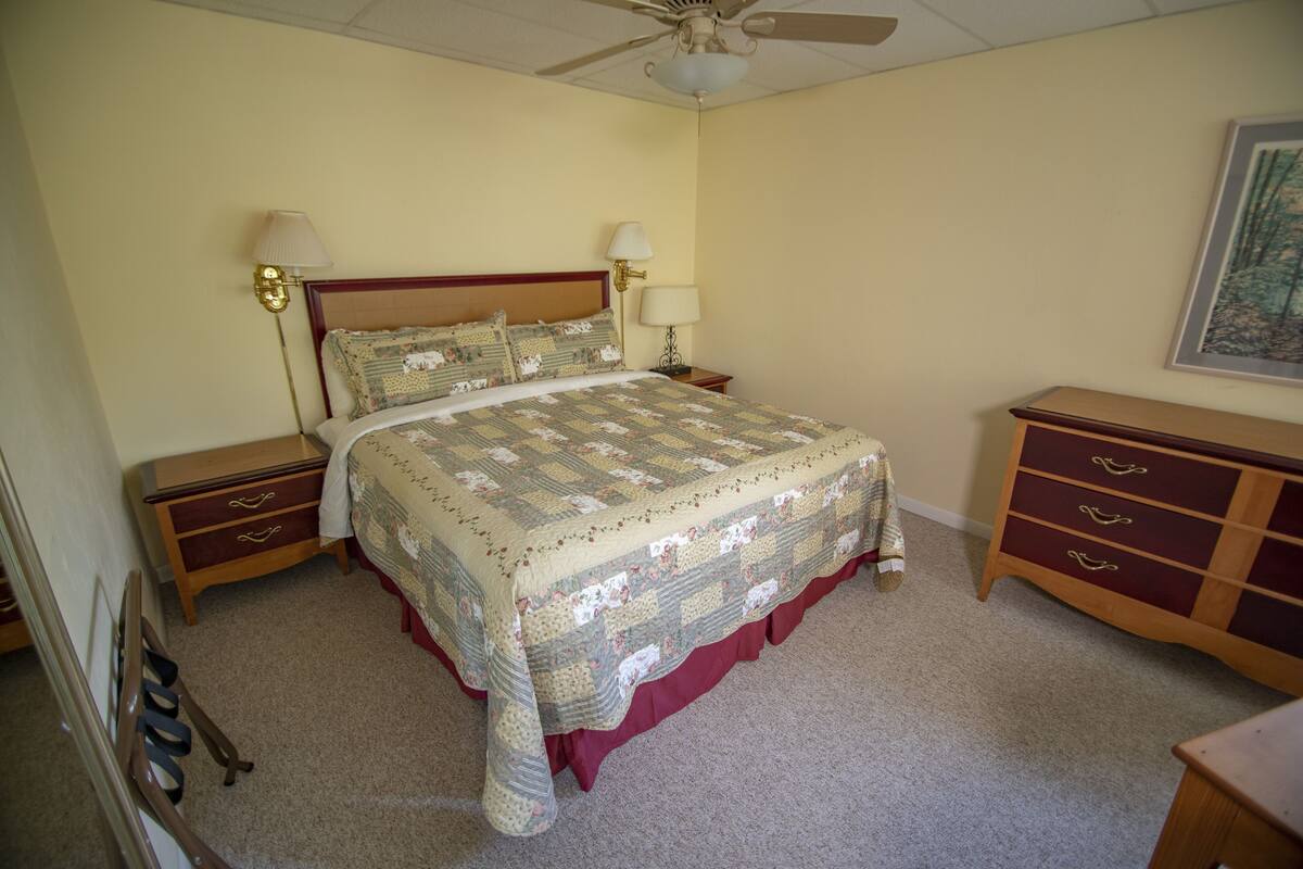 A bedroom with a large bed, two bedside tables, a dresser, and a ceiling fan.