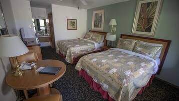 A hotel room with two beds, a desk with a lamp, a chair, and a ceiling fan.