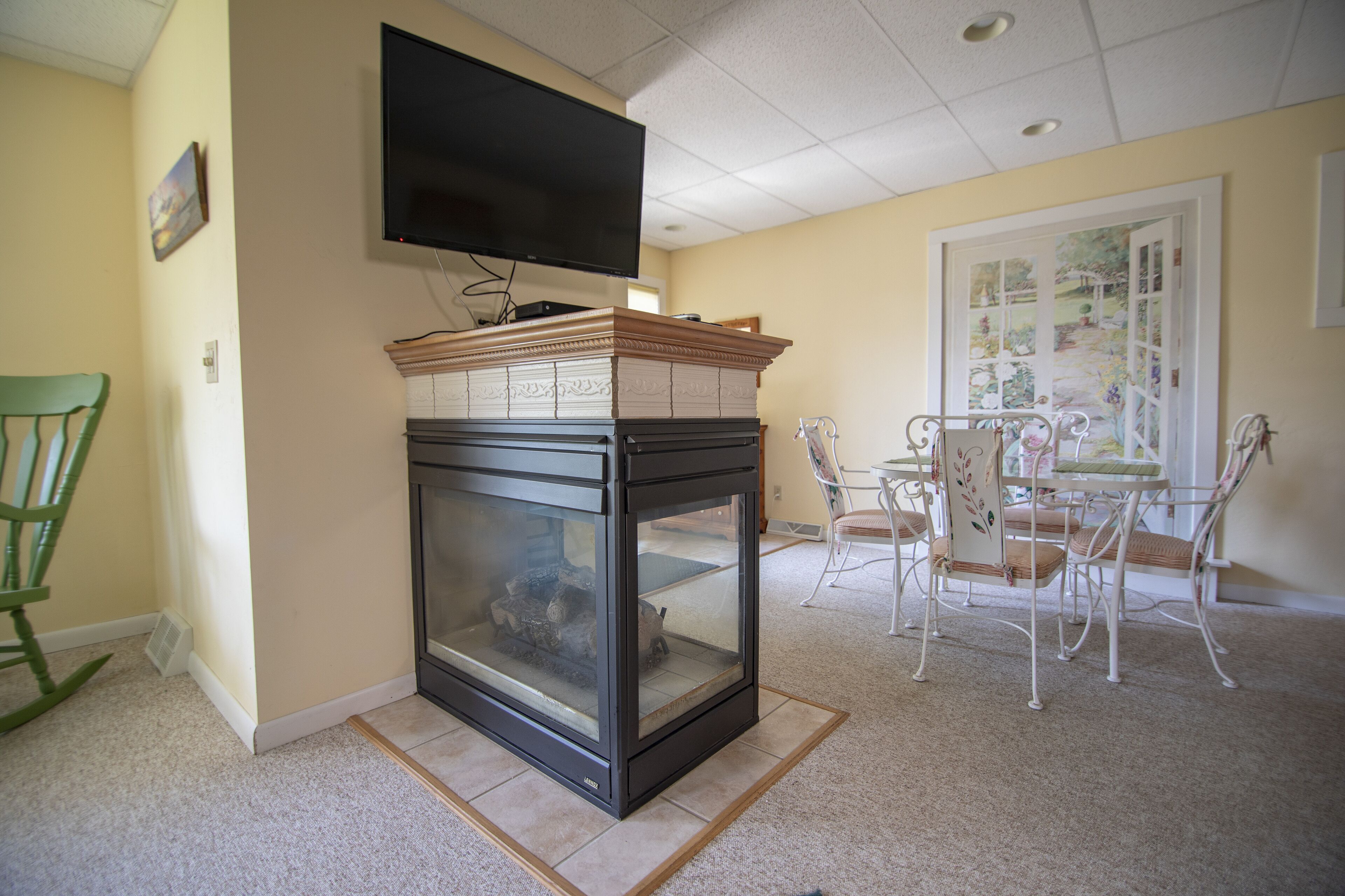 A living room with a fireplace, a television mounted on the wall, and a dining area with a table and chairs.