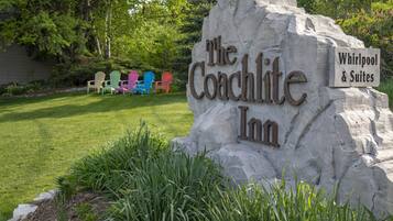 Une enseigne en pierre portant les inscriptions « The Coachlite Inn » et « Whirlpool & Suites », entourée d’une pelouse bien entretenue et de chaises Adirondack aux couleurs vives.